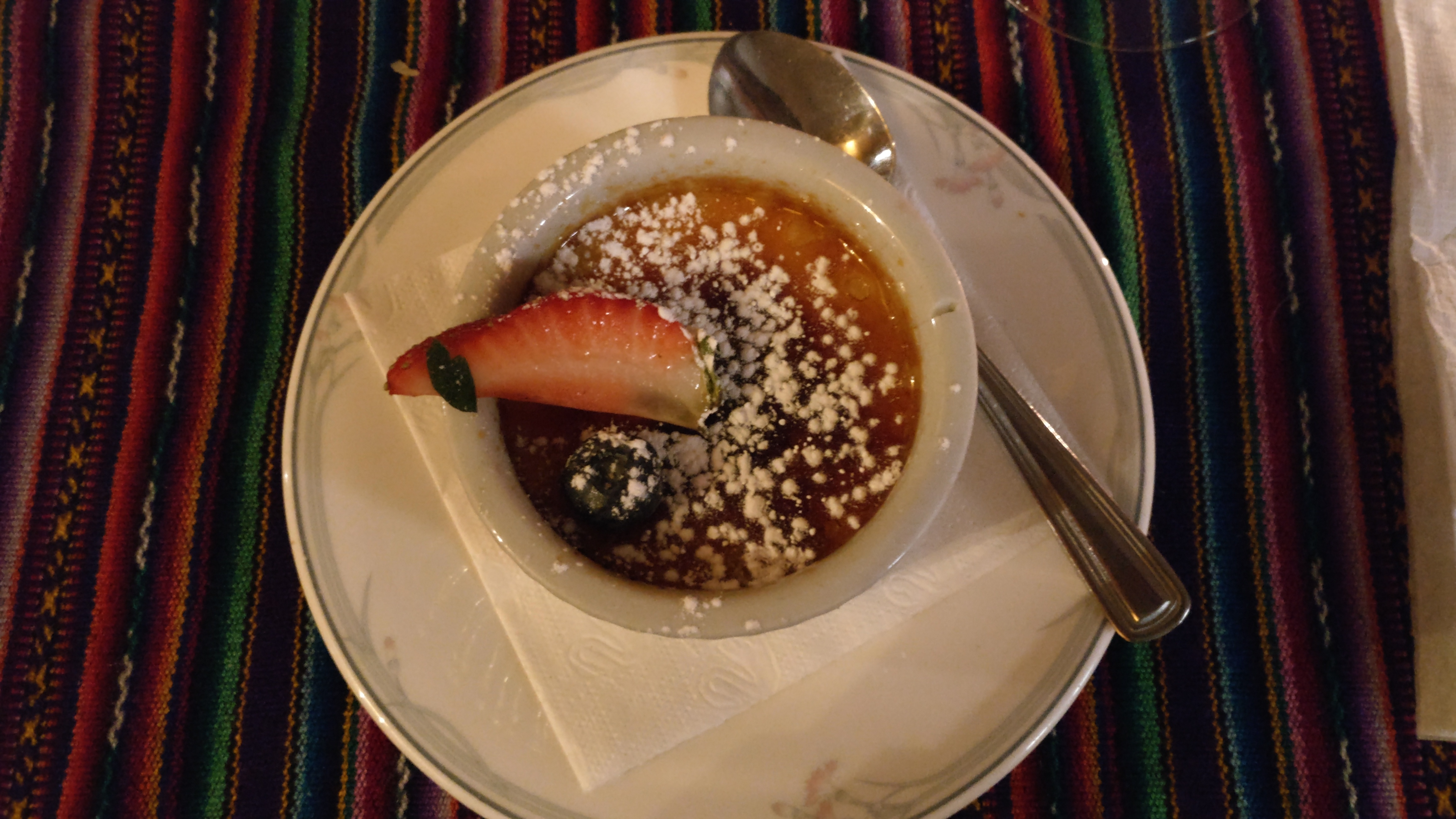 Creme brulée topped with a strawberry wedge, a blueberry, and a dusting of icing sugar